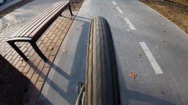 Bir bisikletçi, arka tekere odaklanan bir dikiz aynasından çekilen bir bisiklet yolu boyunca gider. Düz asfalt, işaretli şeritler ve kentsel çevre hareketi ve perspektifi vurguluyor. Dinamik bir çekim.