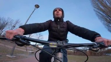 Bir bisikletçi, manzaralı bir parkta yüzlerini net bir şekilde gören bir bisiklet sürüyor. Güneş ışığı ağaçların arasından süzülür, sıcak bir parıltı yayar. Bereketli yeşillik ve dolambaçlı yollar barışçıl ve