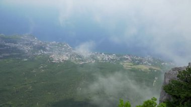 Bir dağın tepesinden sahil kasabasına, alçak bulutlar bir dağ ormanının üzerinde süzülüyor.