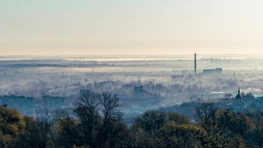 Sabah ışığında Lviv 'in sanayi bölgesinin panoramik görüntüsü, fabrikalar, bacalar, depolar ve demiryolları yumuşak bir gökyüzü altında uzanıyor, kentsel yapıyı sakin şafak atmosferiyle harmanlıyor..