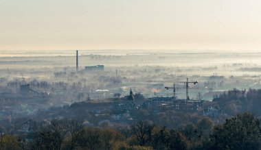 Sabah ışığında Lviv 'in sanayi bölgesinin panoramik görüntüsü, fabrikalar, bacalar, depolar ve demiryolları yumuşak bir gökyüzü altında uzanıyor, kentsel yapıyı sakin şafak atmosferiyle harmanlıyor..