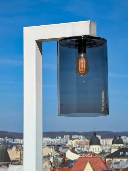 Mavi cam bir gölgeye sahip güzel bir lamba berrak mavi bir gökyüzüne canlı bir şekilde karşı duruyor ve çarpıcı bir görsel karşıtlık oluşturuyor.