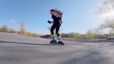 Genç kız güneşli bir günde asfalt yolda paten kayıyor.