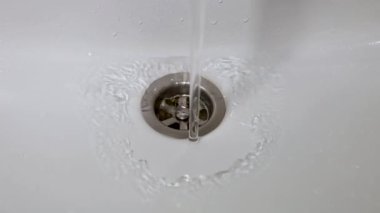 Bir su akıntısı musluktan beyaz lavaboya akıyor.