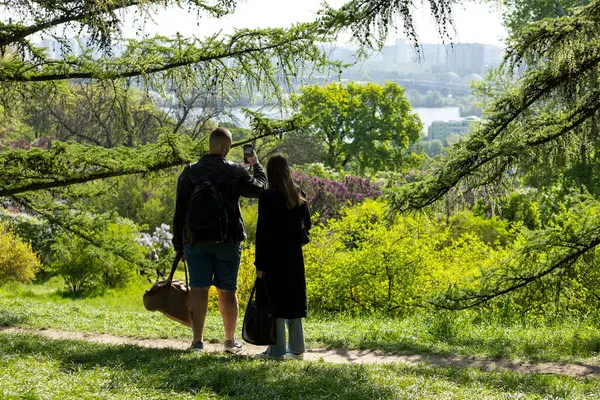 2025.05.01, Kyiv, Ukrayna: Güzel bir parkın kenarında duran iki kişi, çarpıcı şehir manzarasını telefonla çekiyor. Etrafı yeşillik ve açık gökyüzü ile çevrili, sakin manzaraya ve kentsel ufka hayran olmak için durdular..