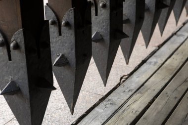 Eski demirden dövülmüş kare hücreli ve ucu sivri uçlu antik bir kafes kapısı. Karmaşık, yıpranmış tasarımı tarih ve ihtiyatlı bir gizemi çağrıştırıyor..