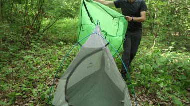 Ormandaki çadırın üzerinden koruyucu branda çeken bir adam.