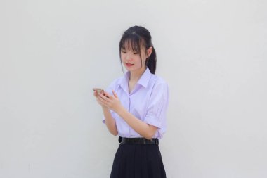 Asya Taylandlı lise öğrencisi üniforması güzel kız telefonunu kullanıyor ve gülümsüyor.