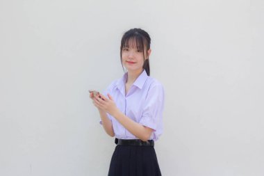 Asya Taylandlı lise öğrencisi üniforması güzel kız telefonunu kullanıyor ve gülümsüyor.