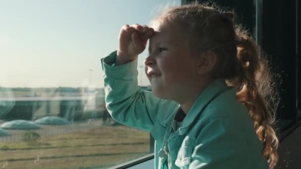 小女孩透过机场候机楼的窗户向外望着一架起飞的飞机 和孩子一起坐飞机的家庭旅行高质量的4K镜头 — 图库视频影像