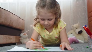 Pretty girl child, lying on the floor, drawing a childs drawing on the paper with floumats. Kids leisure time, childrens art. 4k footage