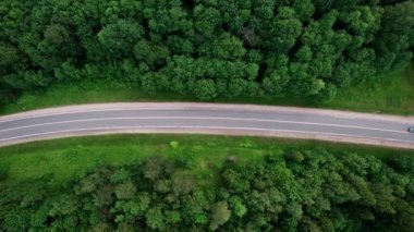 Yeşil yaprak döken bir ormanda, manzaralı bir yolda uçan bir dronun hava görüntüsü. Bir kır yolu boyunca arabayla seyahat etmek. - Evet. Yüksek kalite 4k görüntü