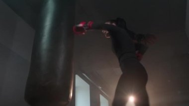 Güçlü, agresif kadın boksör kum torbasına tekme atıyor. Sportif sinirli kadın profesyonel olarak karanlık bir spor salonunda boks yapıyor. Ağır çekim. Güçlü bağımsız kadın kavramı, feminizm. Yüksek kalite 4k