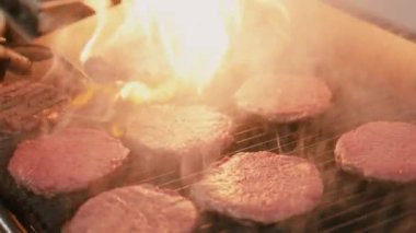Izgaradaki burger için et pişirme işlemi. Sulu et, aşçı eliyle ters çevrilir. Şefin elinin yakın çekimi, ağır çekim. 4k görüntü