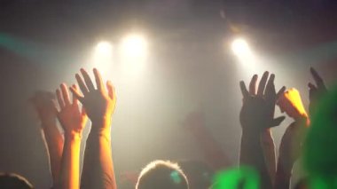 Taraftarlar, bir gece kulübünün sahnesindeki bir müzik grubunun konserinde ellerini havaya kaldırıyorlar. Yavaş çekimde dans eden insanların arka plan görüntüsü. Yüksek kalite 4k görüntü