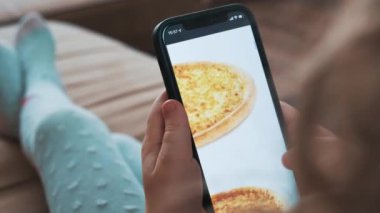 Evde akıllı telefon kullanarak yemek siparişi vermek, yakın plan. Küçük kız akıllı telefondan pizzayı cep telefonuyla seçiyor. Yüksek kalite 4k görüntü