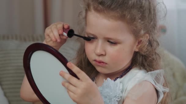かわいい女の子は彼女の目を描き 鏡を見ています 娘は化粧をしながら母親と遊ぶ 赤ちゃんは鏡を見ることによって大人を模倣し 美しさをつけています — ストック動画