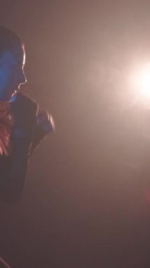 Güzel, güçlü kadın kickboksör tek başına karanlık bir spor salonunda, kum torbasını yavaş çekimde yeniyor. Agresif spor kadın antrenmanı dayanıklılık güçlü çalışma.