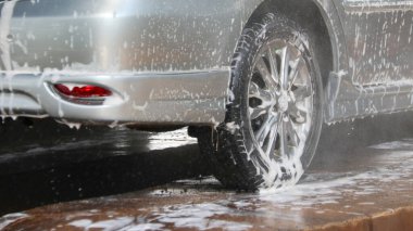 Siyah araba lastiği yıkılıyor ve bir araba bakım evinde köpükle kaplanıyor.                                                       