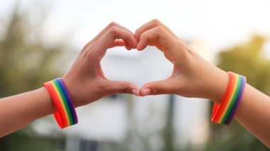 LGBT gurur konseptinde aşkı göstermek için kalp işareti yapan ellerde gökkuşağı bileklikleri var.                       