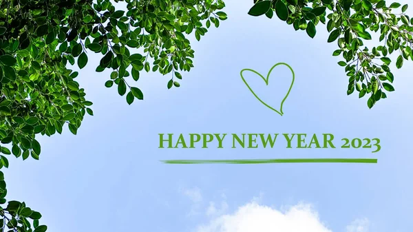 Green text happy new year 2023 with green heart on blue sky and green leaves background concept for greeting and welcoming new year 2023