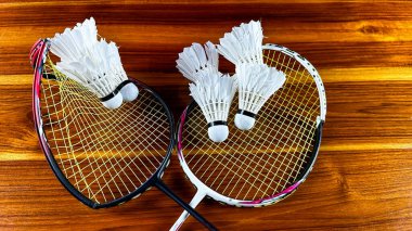 Close up of broken badminton rackets and white badminton shuttle cocks on brown wooden background