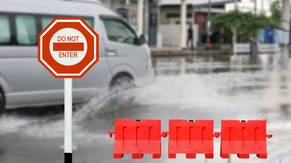 Red traffic sign with graphic of warning do not enter due to flood and red road barriers on blurred flooded street background