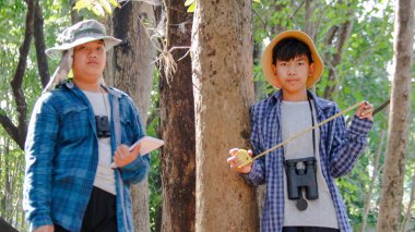 Genç Asyalı çocuklar, yerel bir parkta, yumuşak ve seçici bir odak noktası olan bir ağacı ölçmek için mezura kullanıyorlar.