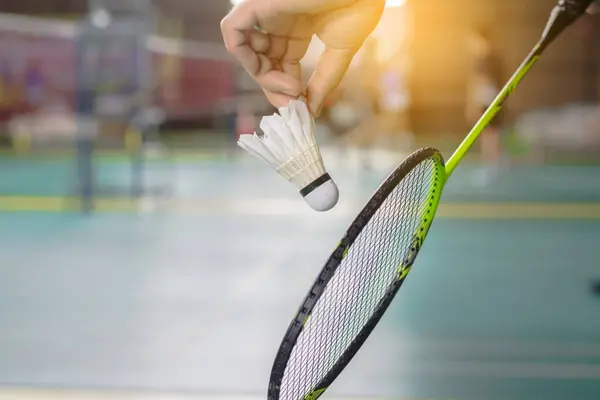 Badminton oyuncusu elinde beyaz bir horoz ve raket tutuyor ve ağda hazır bekliyor..