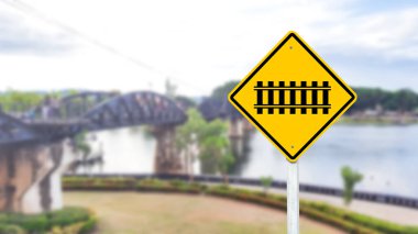 Parlak sarı bir tabela üzerinde siyah bir demiryolu geçiş sembolü belirgin bir şekilde sergilenmektedir. Bu uyarı işareti, sürücüleri ve yayaları önümüzdeki demiryolu geçidine karşı uyarır. Bölgede güvenlik ve ihtiyatın arttırılması.
