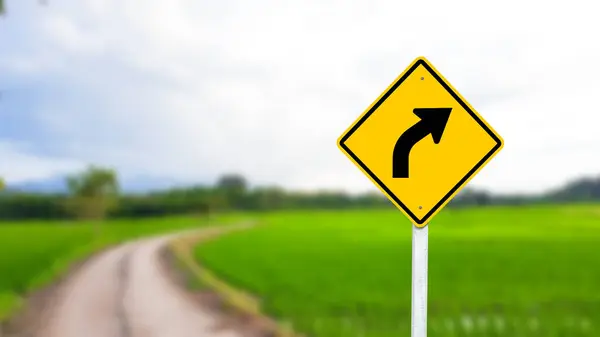 stock image A black right-curved arrow is displayed on a bright yellow sign. The bold arrow indicates a right turn ahead, ensuring drivers are aware of the upcoming change in direction. The vivid yellow background enhances visibility for safe navigation.