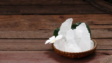 Beyaz alum kristalleriyle dolu bir sepet canlı yeşil bir çalı arka planında duruyor. Çelişkili renkler, mezunların yemyeşil alanlara karşı saflığını vurguluyor ve taze bir his yaratıyor..