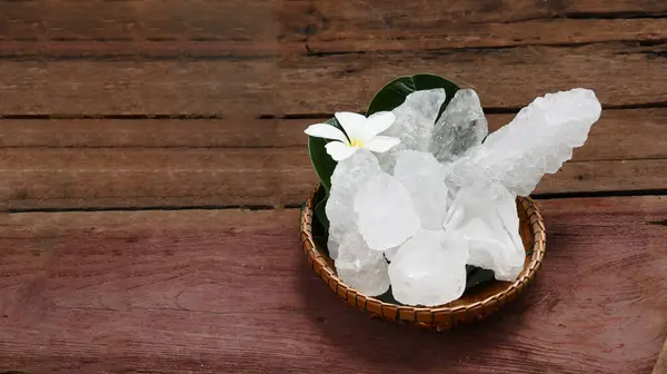 stock image A basket filled with white alum crystals sits on a vibrant green shrub background. The contrasting colors highlight the purity of the alum against the lush greenery, creating fresh feeling.