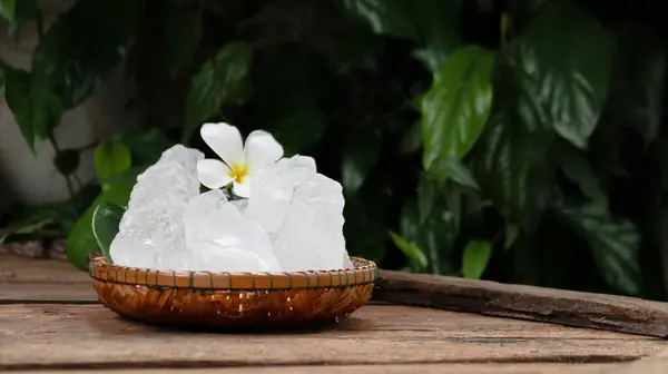 stock image A basket filled with white alum crystals sits on a vibrant green shrub background. The contrasting colors highlight the purity of the alum against the lush greenery, creating fresh feeling.