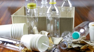 Beyaz kağıt kahve fincanı, kullanılmış kağıt, plastik şişeler ve kahverengi bir yüzey üzerinde geri dönüşümü bekleyen karton kutu. Atıkların geri dönüşümünü teşvik eder, Dünya 'yı kurtarır ve doğal kaynakları korur..
