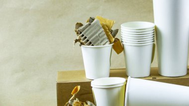 Beyaz kağıt kahve fincanı, kullanılmış kağıt ve kahverengi bir yüzey üzerinde geri dönüşümü bekleyen karton kutu. Atıkların geri dönüşümünü teşvik eder, Dünya 'yı kurtarır ve doğal kaynakları korur..