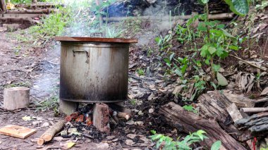 Alev fırınında kaynayan, dumanlı paslanmaz çelik tencerenin görüntüsü. Geleneksel yemek pişirme yöntemlerinin özünü yakalar..