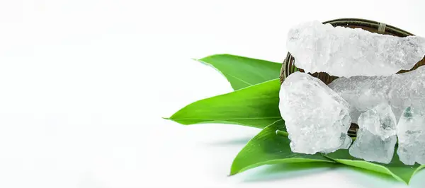 stock image Clear and pristine alum cubes resting in a bamboo basket alongside leaves, set against a white background, showcasing the natural purity and traditional presentation of the substance.