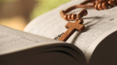 Koyu kahverengi ahşap haç eski açık bir kitabın üzerinde Hristiyanlar arasında İsa 'nın sevgisinin yayılmasını simgeliyor. İnanç bağlılığını ve Hıristiyan öğretilerinin önemini yansıtıyor..