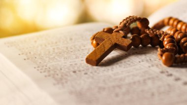 Koyu kahverengi ahşap haç eski açık bir kitabın üzerinde Hristiyanlar arasında İsa 'nın sevgisinin yayılmasını simgeliyor. İnanç bağlılığını ve Hıristiyan öğretilerinin önemini yansıtıyor..