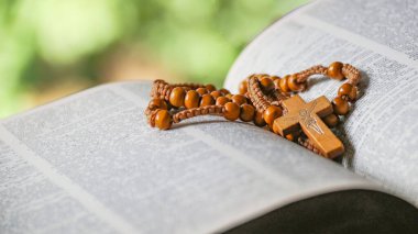Koyu kahverengi ahşap haç eski açık bir kitabın üzerinde Hristiyanlar arasında İsa 'nın sevgisinin yayılmasını simgeliyor. İnanç bağlılığını ve Hıristiyan öğretilerinin önemini yansıtıyor..