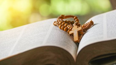 Koyu kahverengi ahşap haç eski açık bir kitabın üzerinde Hristiyanlar arasında İsa 'nın sevgisinin yayılmasını simgeliyor. İnanç bağlılığını ve Hıristiyan öğretilerinin önemini yansıtıyor..