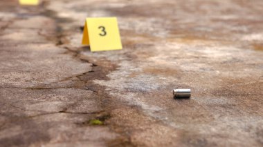 Yerde 3 numaralı bulanık işaretle boş bir mermi kovanı var. Spor ve güvenlik kavramları hem rekabetçi spor hem de koruyucu tedbirlerde ateşli silahların çifte doğasını vurguluyor.