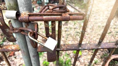Parlak gümüş kilit yastığı eski, paslı bir zincire tutunur. Yeni ve eski metaller arasındaki zıtlığı yakalar. Güvenliği, erişimi ve zamanın geçişini sembolize eder..