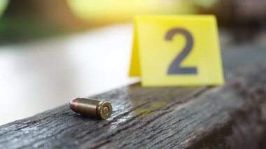 9 mm 'lik bakır mermi koyu ahşap bankta duruyor. Arka planda 2 numaralı bulanık tabela var. Ceza soruşturmaları ve atış sporu kavramları.