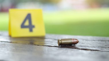 9 mm 'lik tabanca mermisi koyu ahşap bankta duruyor. Arkaplanda 4 numaralı bulanık tabela var. Ceza soruşturmaları ve atış sporu kavramları.