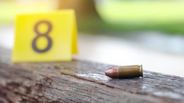 9 mm 'lik tabanca mermisi koyu ahşap bankta duruyor. Arkaplanda 8 numaralı bulanık tabela var. Ceza soruşturmaları ve atış sporu kavramları.