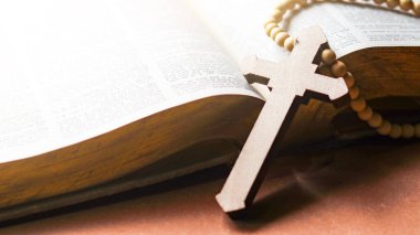 Kahverengi ahşap haç eski açık bir kitabın üzerinde Hristiyanlar arasında İsa 'nın sevgisinin yayılmasını simgeliyor. İnanç bağlılığını ve Hıristiyan öğretilerinin önemini yansıtıyor..