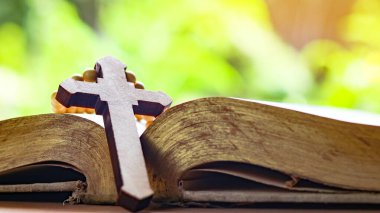 Kahverengi ahşap haç eski açık bir kitabın üzerinde Hristiyanlar arasında İsa 'nın sevgisinin yayılmasını simgeliyor. İnanç bağlılığını ve Hıristiyan öğretilerinin önemini yansıtıyor..