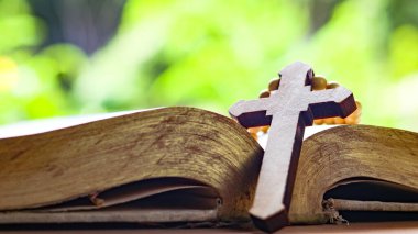 Kahverengi ahşap haç eski açık bir kitabın üzerinde Hristiyanlar arasında İsa 'nın sevgisinin yayılmasını simgeliyor. İnanç bağlılığını ve Hıristiyan öğretilerinin önemini yansıtıyor..